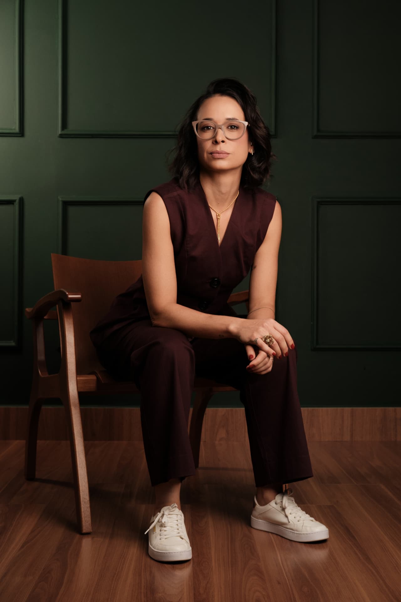 Aline Carrijo sentada em poltrona diante de fundo verde